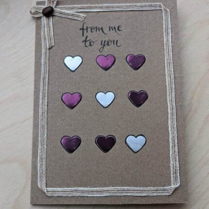 Elegant handmade Valentine's Day card featuring purple and white paper hearts, lying on a table. Made in Bollington, UK.