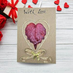Handmade Valentine’s Day card featuring a heart crafted from dried red leaf, cotton string and golden bow.